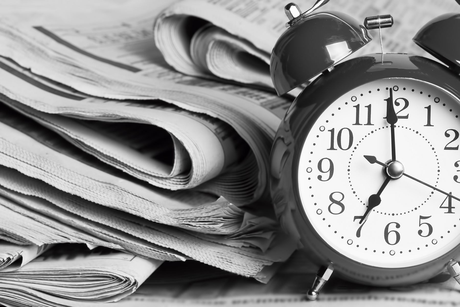 Newspapers stacked next to an alarm clock