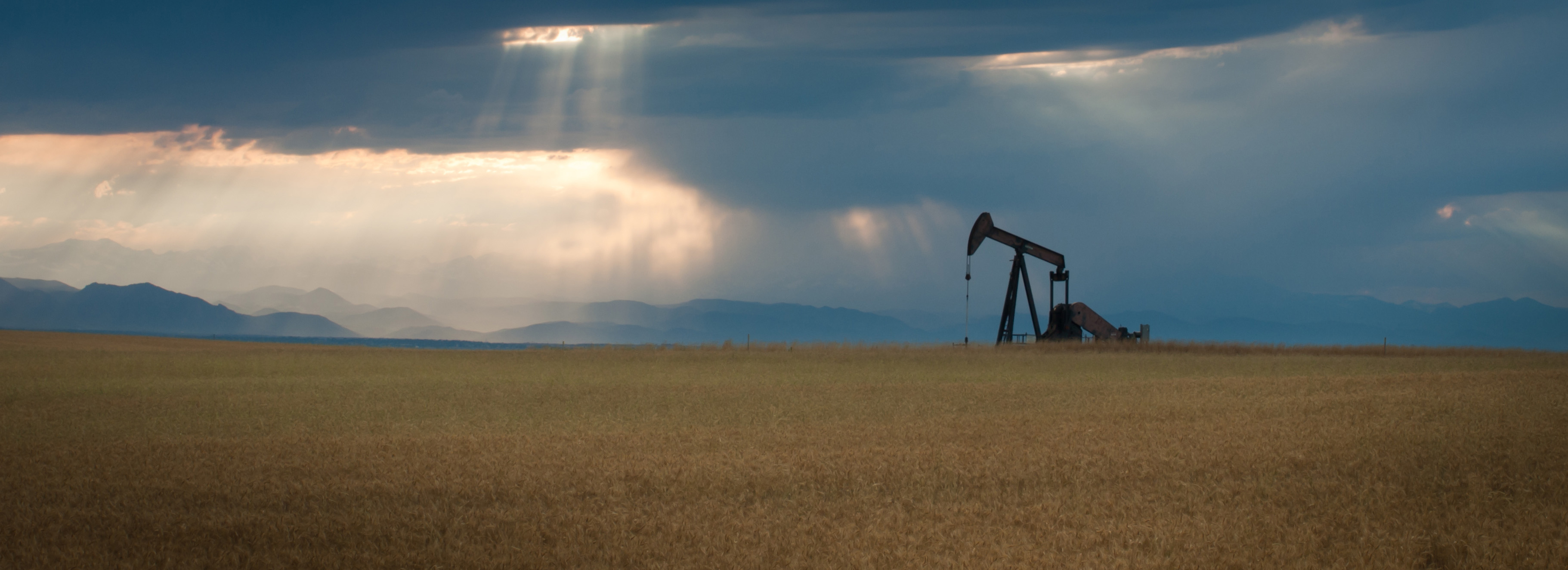 Oil Derrick on wheat field with a cloudy sky in the background. The sun is shining through the clouds